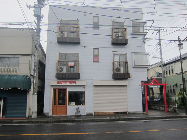 千葉県道1号市川松戸線沿いに建つ白いマンションの1階にある。