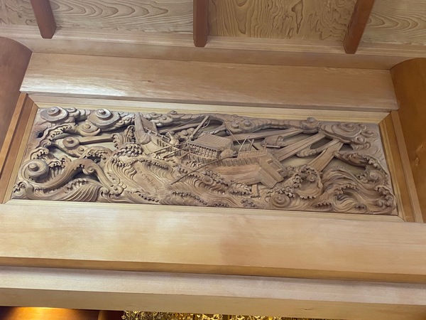 欄間の一部。海上題目(1271年/文永8年)日蓮聖人51歳。本土から佐渡へ流刑になった時、大荒れの海に日蓮聖人が“南無妙法蓮華経”と書いたところ、波は穏やかになり無事佐渡に着いた。荒波に文字を記す日蓮聖人の姿を顕している。